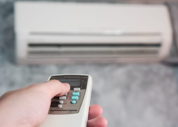Hand holding remote in front of air conditioner.